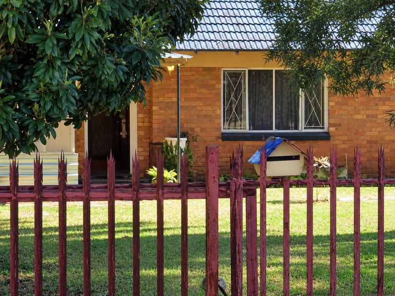 Front view of a brick house featuring a tiled roof, security window bars, and a metal perimeter fence.