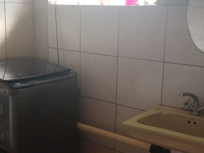 A functional laundry area featuring a utility sink and tiled splashback, requiring some cosmetic updates to improve its overall condition.