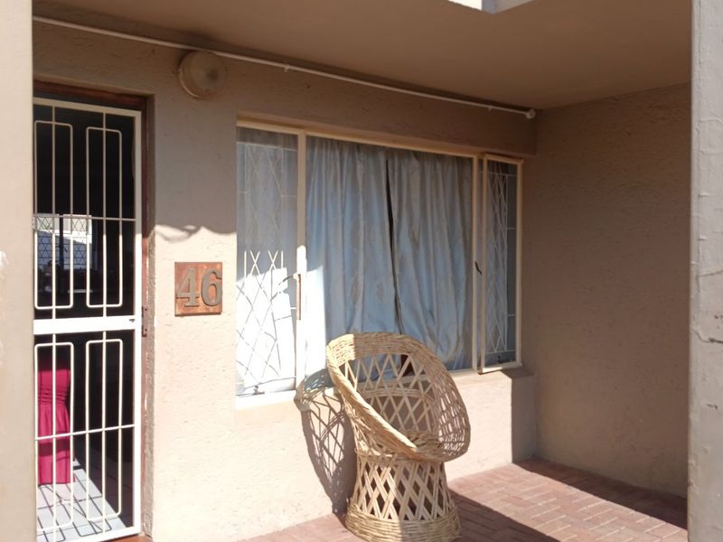 Front entrance area of the apartment featuring brick paving, a security gate, and window security bars.