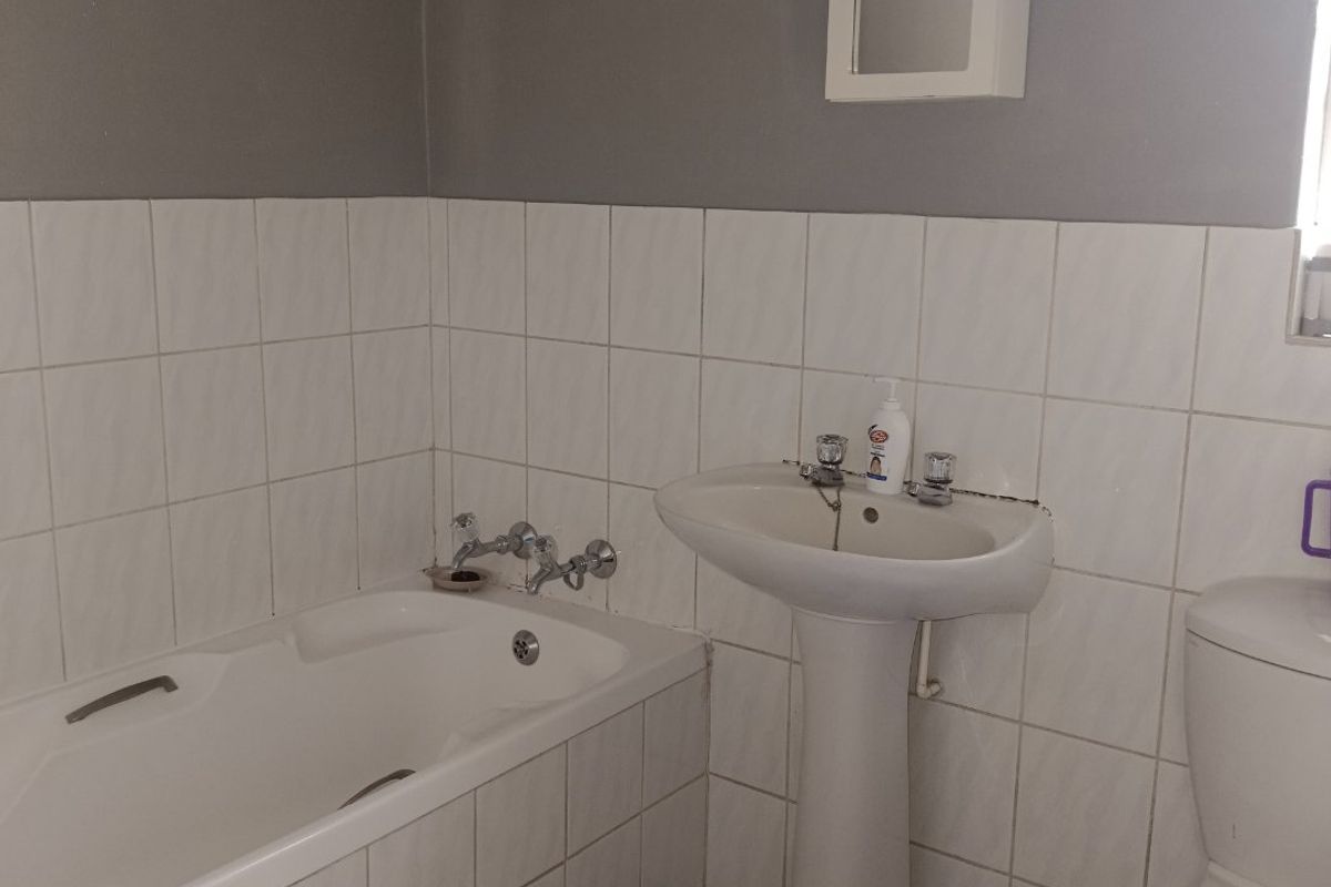 A functional bathroom featuring a pedestal washbasin, built-in bathtub, and dual-flush toilet with neutral wall and floor tiling.