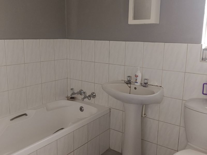 A functional bathroom featuring a pedestal washbasin, built-in bathtub, and dual-flush toilet with neutral wall and floor tiling.