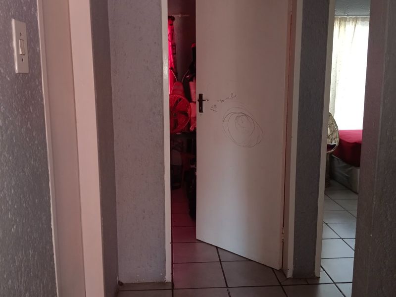 A functional hallway featuring tiled flooring and access to adjacent rooms, currently showing signs of wear and surface markings on the door.