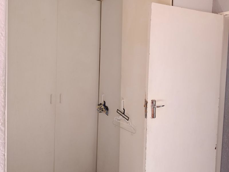 A bedroom corner featuring built-in cupboards with tiled flooring, showing signs of wear and requiring cosmetic updates.