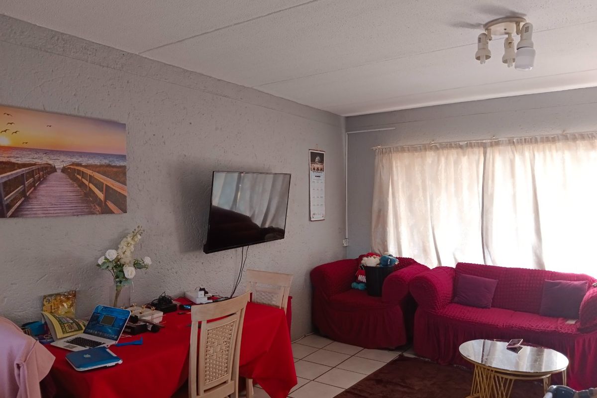 A living room area featuring tiled flooring, textured walls, and a ceiling-mounted light fixture, providing a functional space for relaxation.
