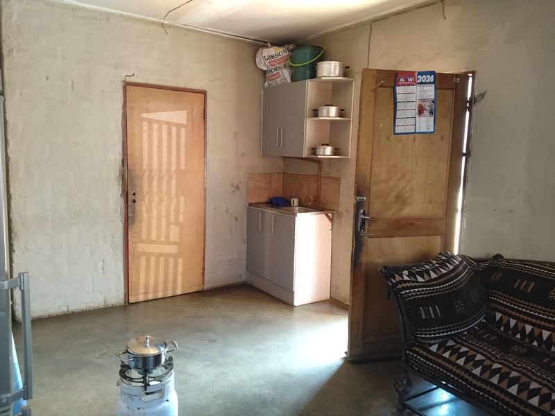 A basic kitchen area featuring compact cabinetry, a sink, and tiled splashback, requiring cosmetic updates to improve the overall finish and functionality.