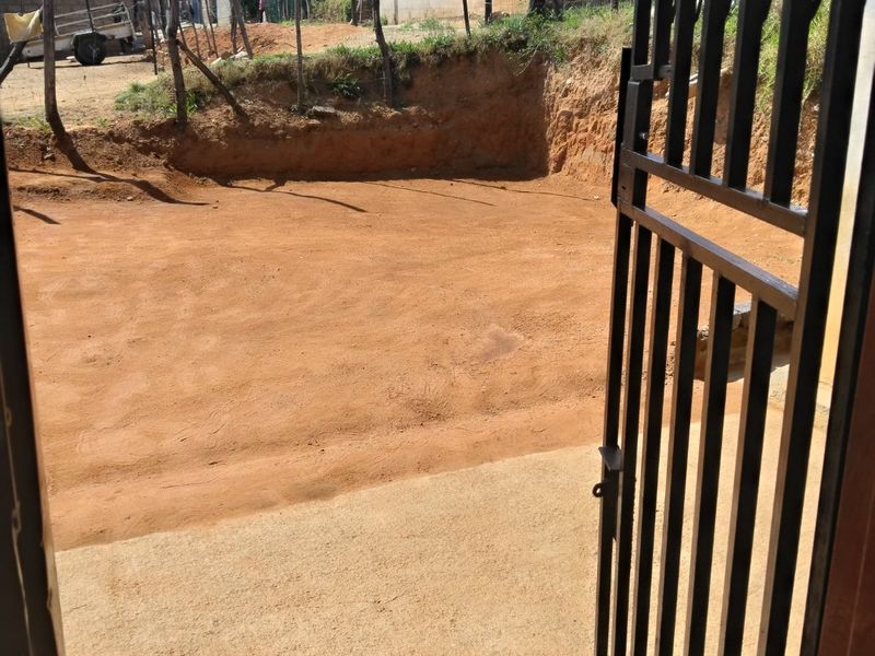 View from a metal security gate looking out onto an unpaved earth yard and driveway area.
