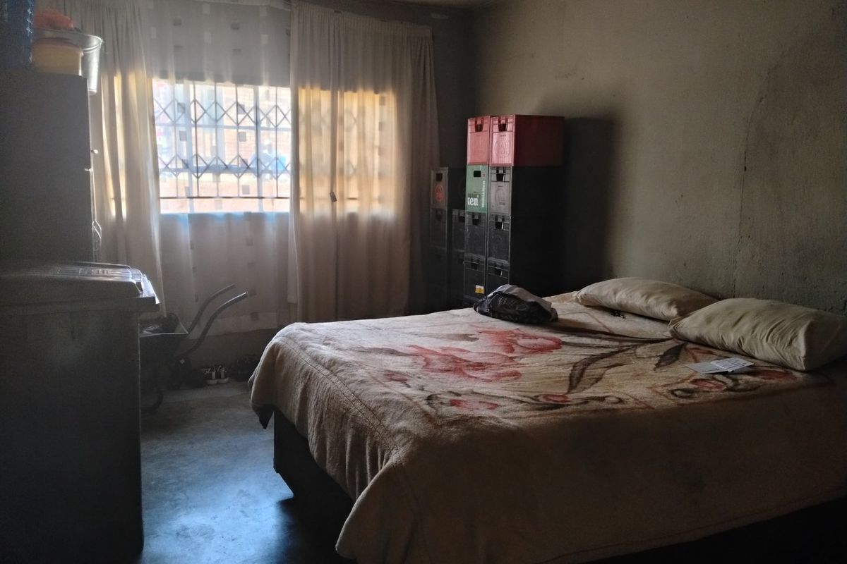 A bedroom featuring a window with a security gate and plain wall finishes, requiring cosmetic updates to improve the overall condition.