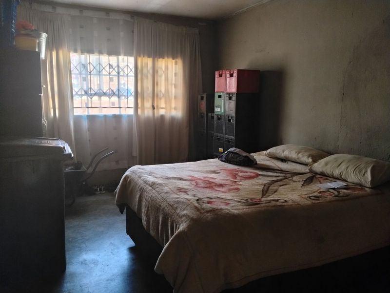 A bedroom featuring a window with a security gate and plain wall finishes, requiring cosmetic updates to improve the overall condition.