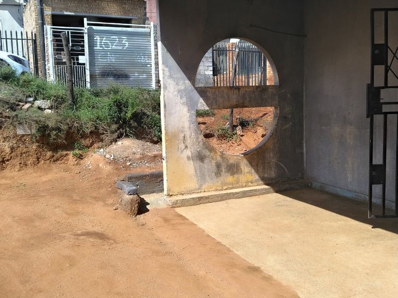Front entrance area featuring a concrete porch and a distinctive circular architectural wall cutout, requiring landscaping and exterior maintenance.