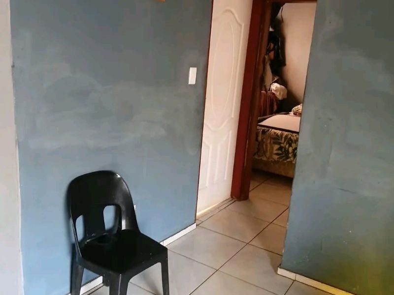 A hallway area featuring tiled flooring and access to an adjoining room, showing signs of wear on the wall surfaces.