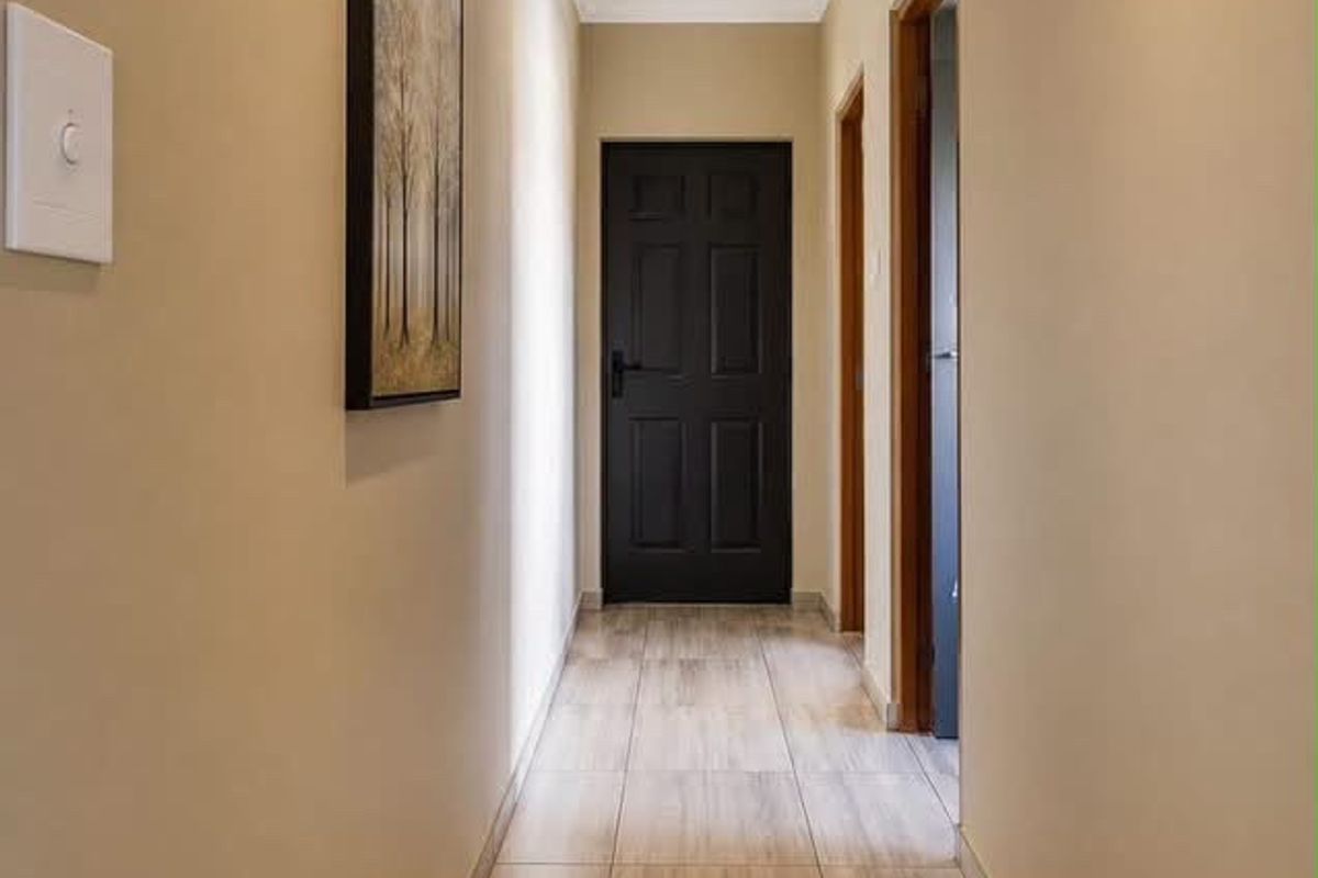 A clean, well-lit hallway featuring modern tiled flooring, recessed ceiling lighting, and neutral wall finishes leading to internal doors.