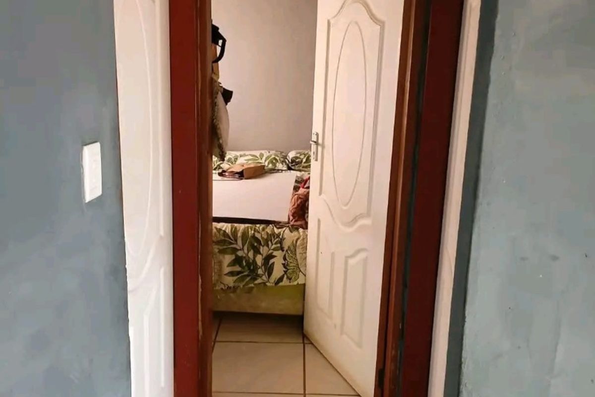 A narrow hallway featuring tiled flooring and white panel doors leading into a bedroom area, showing signs of wear on the door frames.