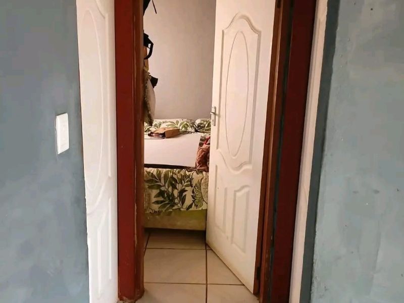 A narrow hallway featuring tiled flooring and white panel doors leading into a bedroom area, showing signs of wear on the door frames.