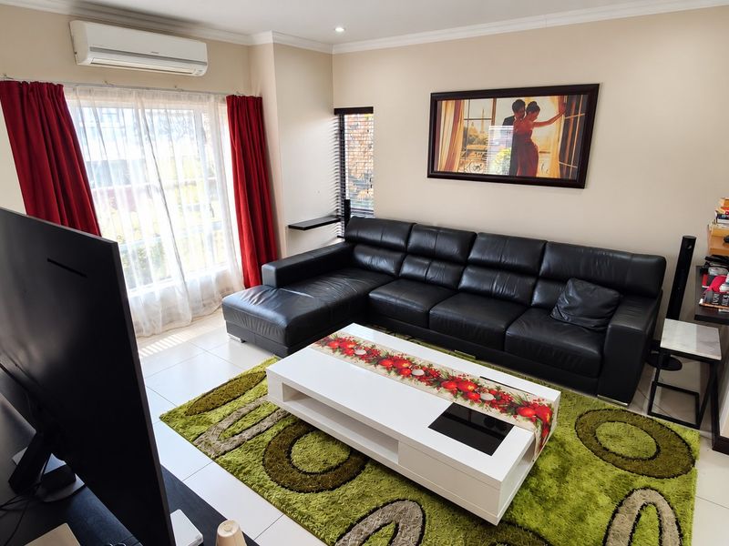 A well-maintained living room featuring tiled flooring, recessed downlighting, and a wall-mounted split-system air conditioning unit.