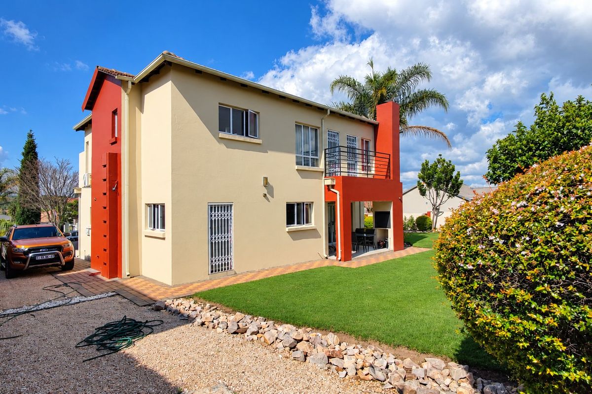 Rear view of a two-story residential property featuring a covered patio, balcony, and well-maintained garden area.