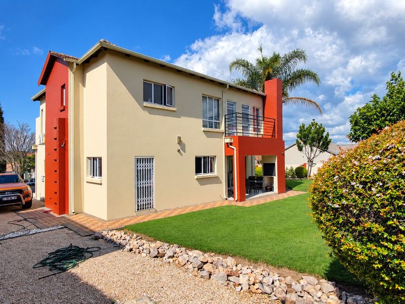 Rear view of a two-story residential property featuring a covered patio, balcony, and well-maintained garden area.