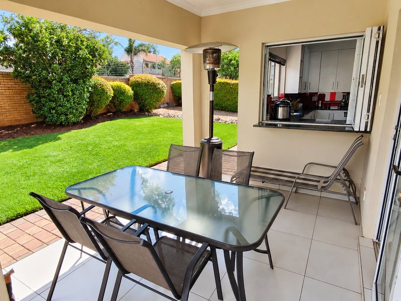 A covered patio featuring tiled flooring and a convenient pass-through window connecting to the kitchen, overlooking a well-maintained garden.