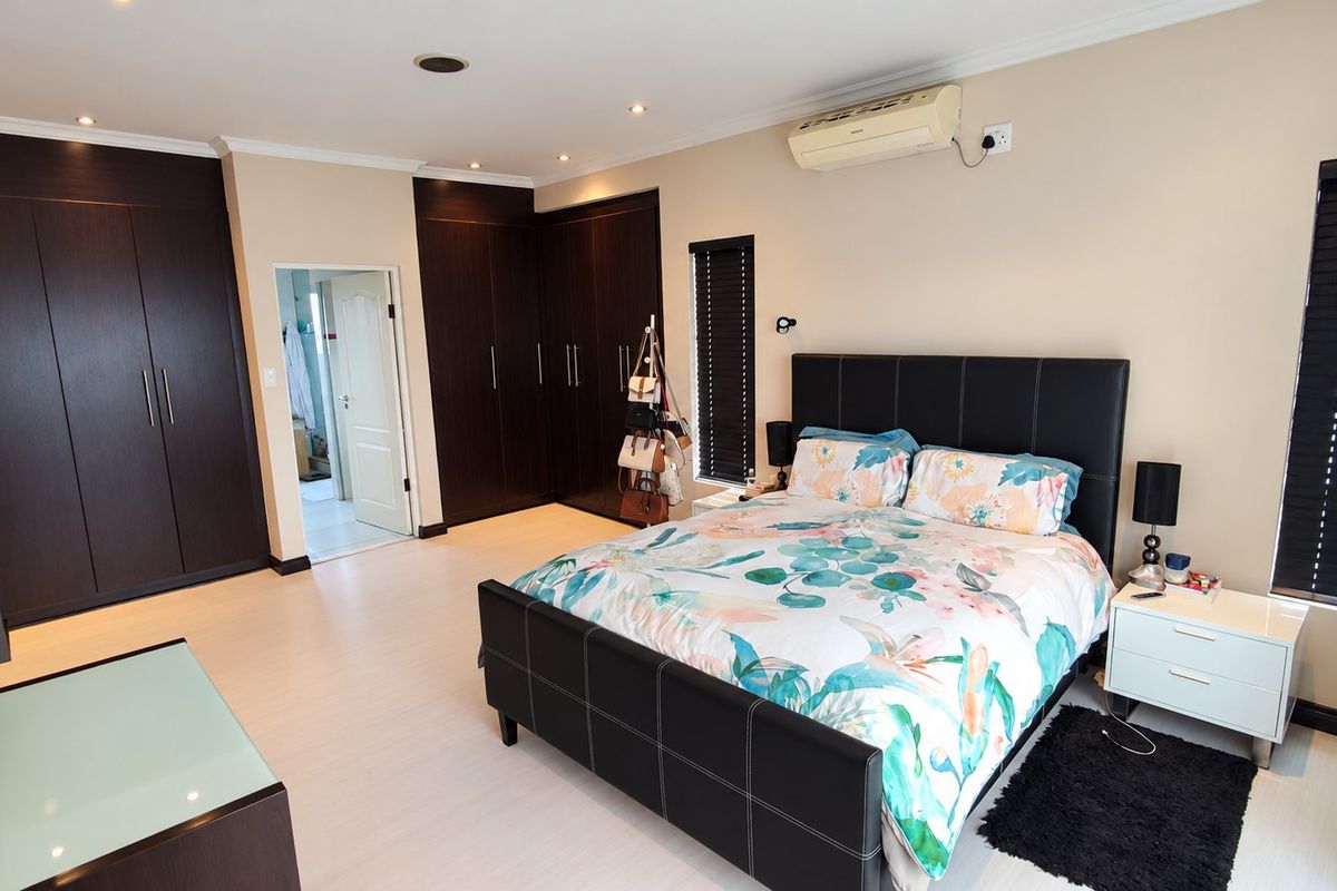 Spacious bedroom featuring extensive dark wood built-in cupboards, recessed lighting, and a wall-mounted air conditioning unit.