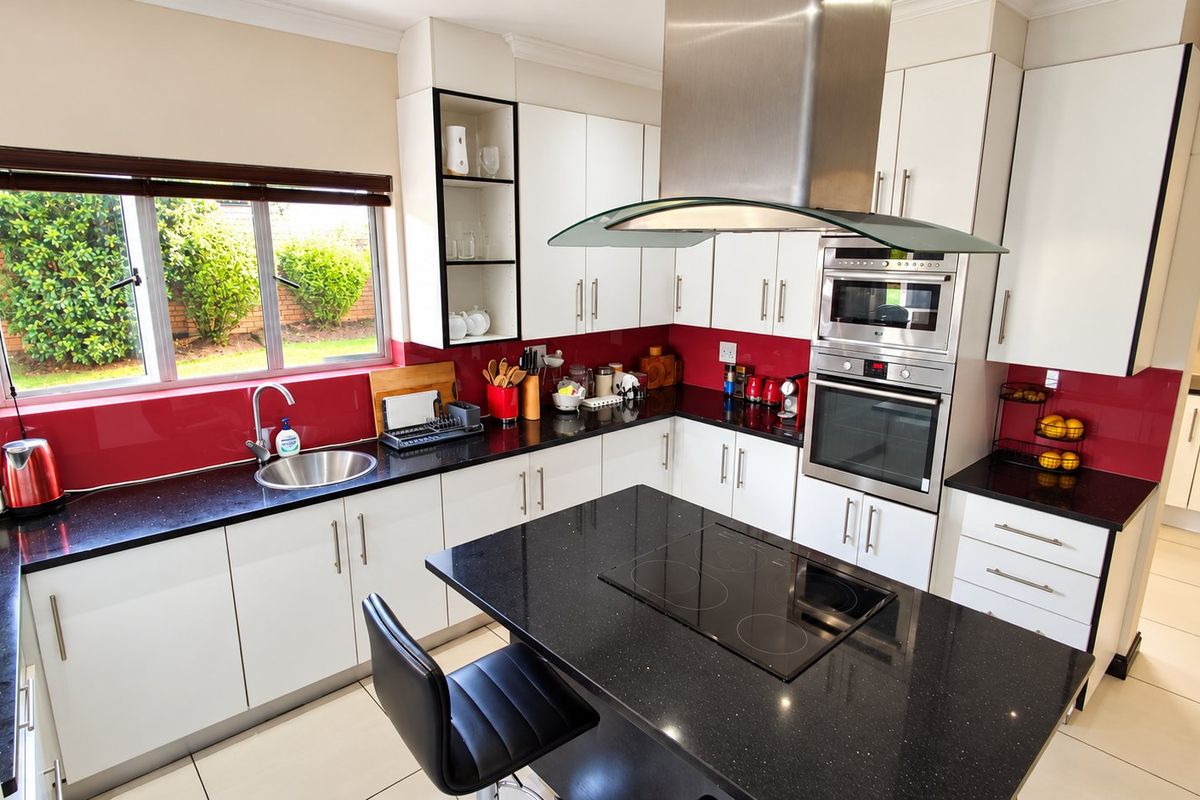 Modern kitchen featuring white cabinetry, black granite countertops, a central island with an electric hob, and integrated stainless steel appliances.