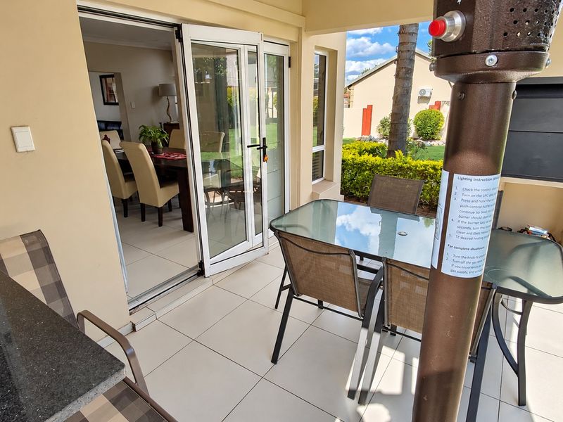 Covered patio area featuring tiled flooring, a built-in braai, and direct access to the interior living space through double glass doors.