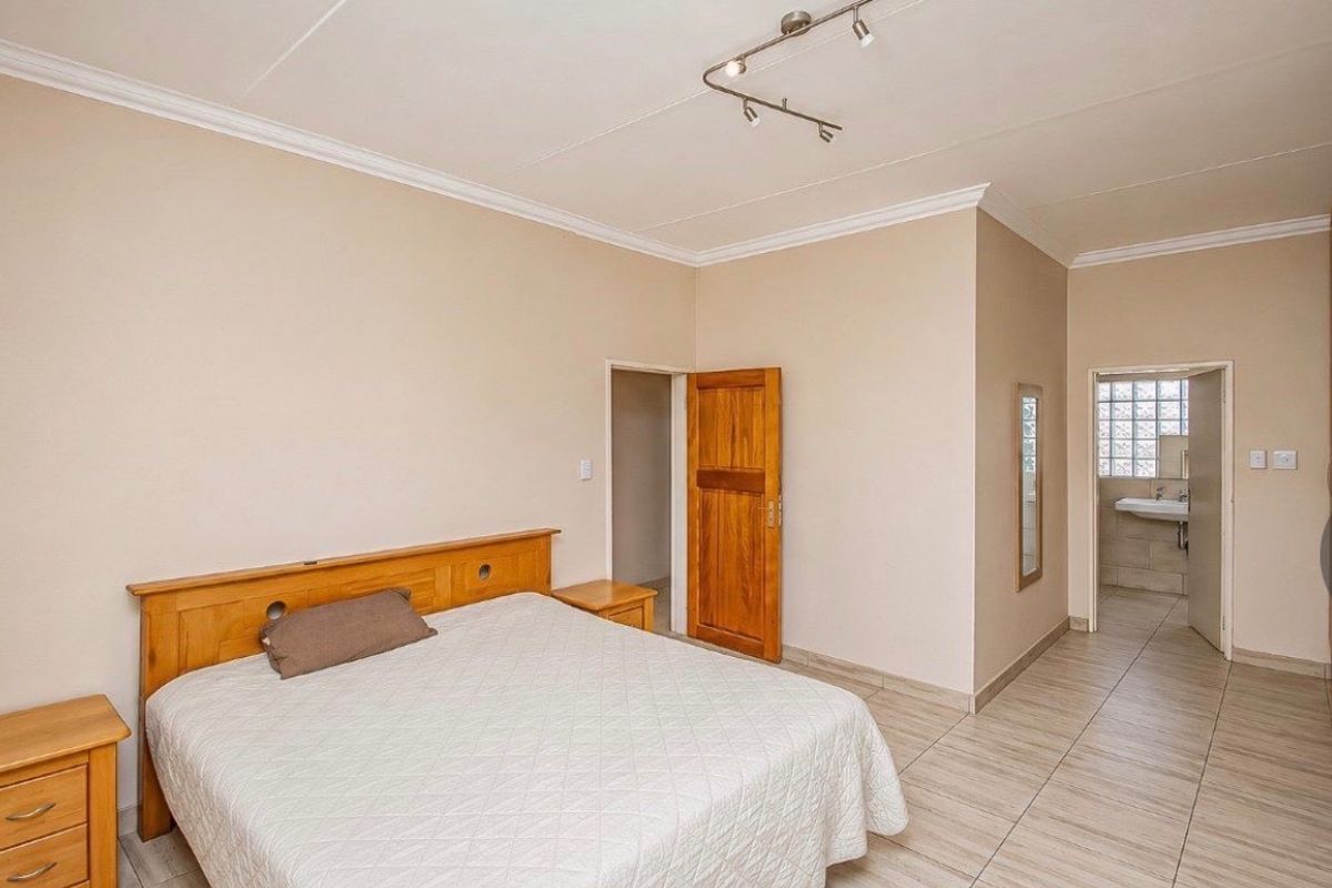Spacious bedroom featuring neutral walls, tiled flooring, track lighting, and an en-suite bathroom with a glass block window.
