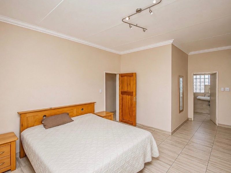 Spacious bedroom featuring neutral walls, tiled flooring, track lighting, and an en-suite bathroom with a glass block window.