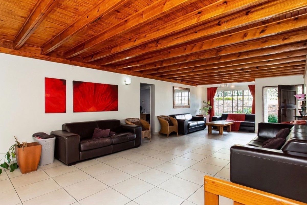 Spacious living area featuring a distinctive exposed timber beam ceiling and neutral tiled flooring, offering a bright and open layout with direct outdoor access.