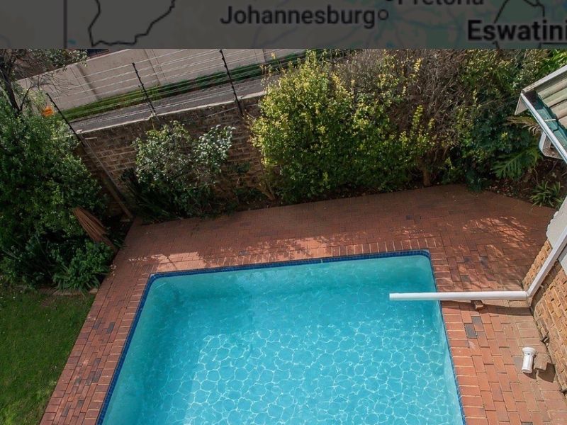 An elevated view of a private swimming pool area featuring brick paving, surrounding garden landscaping, and a secure boundary wall with electric fencing.