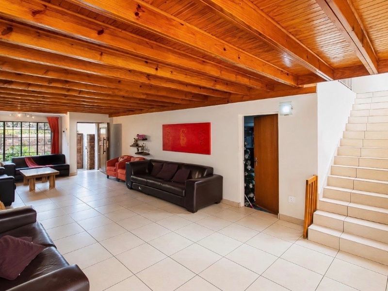 Spacious living area featuring a distinctive exposed timber beam ceiling, neutral tiled flooring, and an internal staircase leading to the upper level.