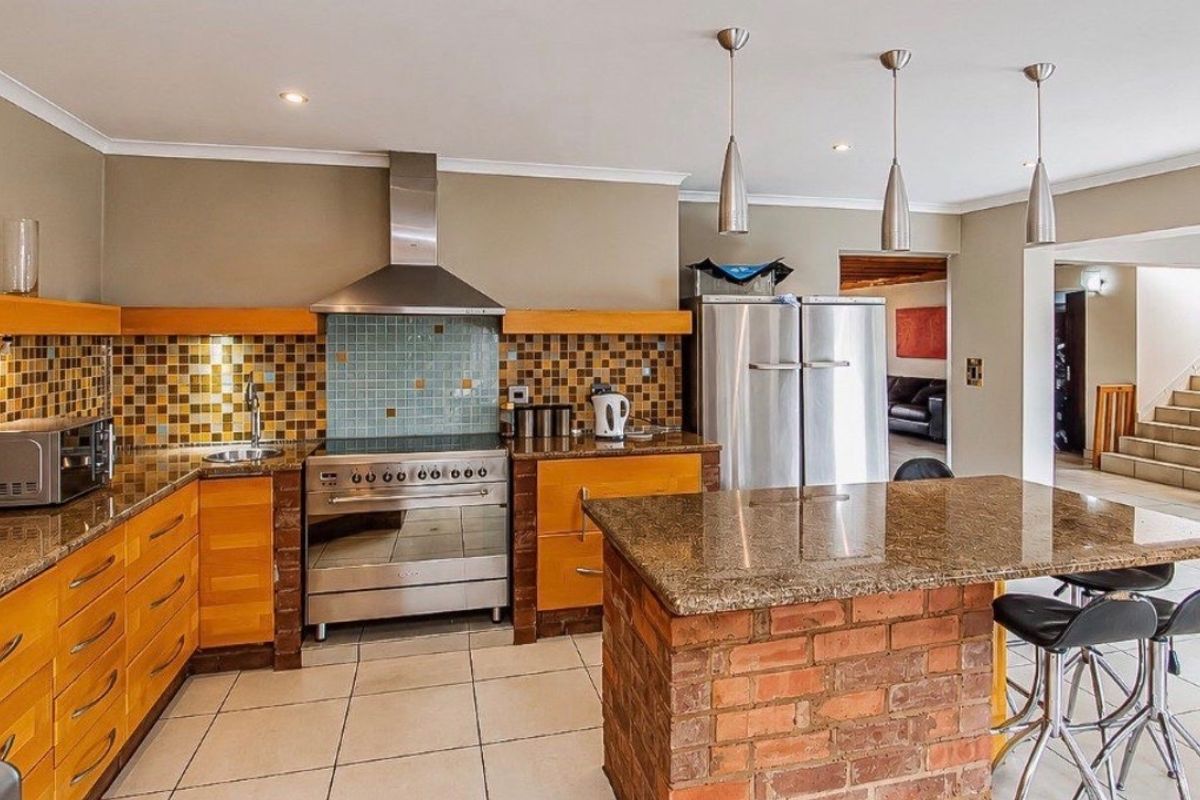 Spacious kitchen featuring granite countertops, a brick-based island, stainless steel appliances, and a decorative mosaic tile backsplash.