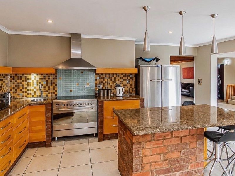 Spacious kitchen featuring granite countertops, a brick-based island, stainless steel appliances, and a decorative mosaic tile backsplash.