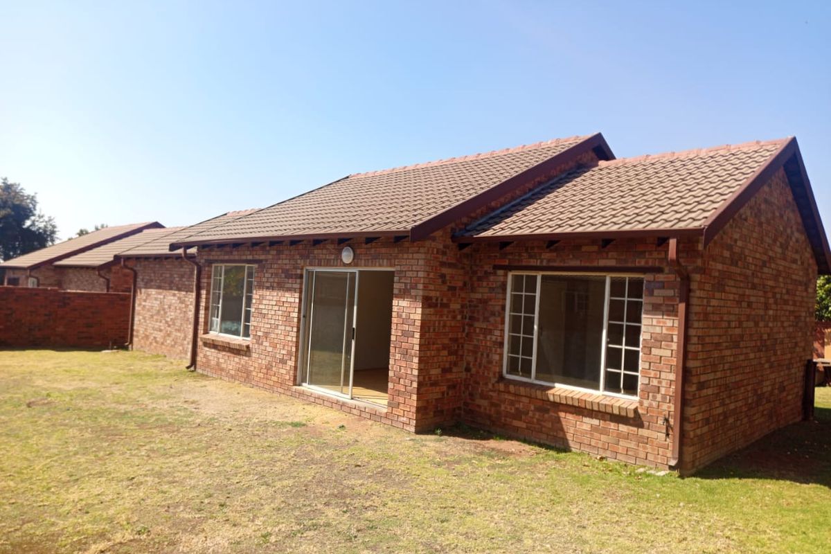 Rear view of a face brick townhouse featuring a tiled roof, sliding glass door access, and grid-pattern windows overlooking a private garden area.