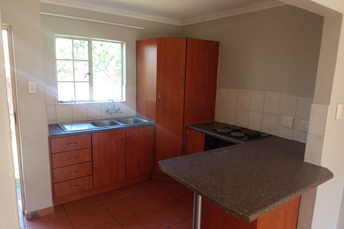 A functional kitchen featuring wooden cabinetry, a double bowl sink, built-in hob, and a breakfast bar with tiled flooring and backsplash.