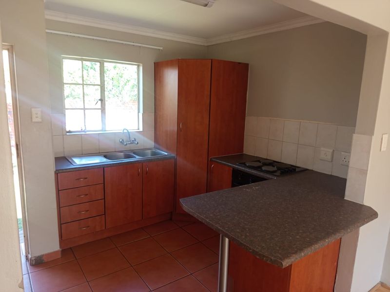 A functional kitchen featuring wooden cabinetry, a double bowl sink, built-in hob, and a breakfast bar with tiled flooring and backsplash.