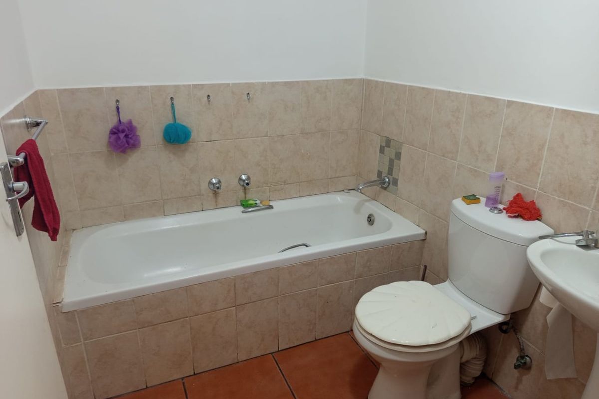 A functional bathroom featuring a built-in bathtub, standard toilet, and washbasin with neutral wall tiling and terracotta-style floor tiles.