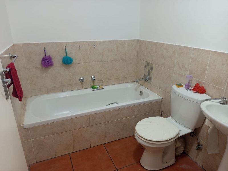 A functional bathroom featuring a built-in bathtub, standard toilet, and washbasin with neutral wall tiling and terracotta-style floor tiles.