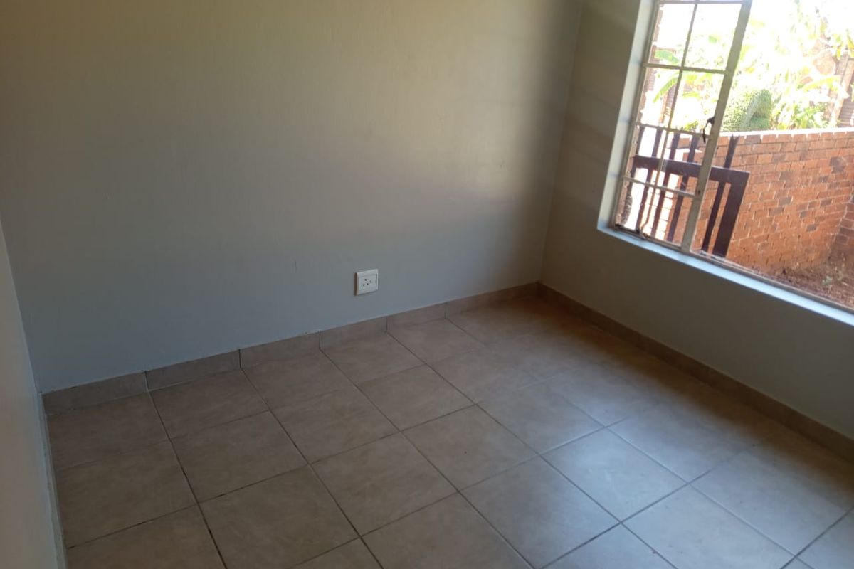 An empty bedroom featuring tiled flooring and a window with security bars, providing a blank canvas for personalization.