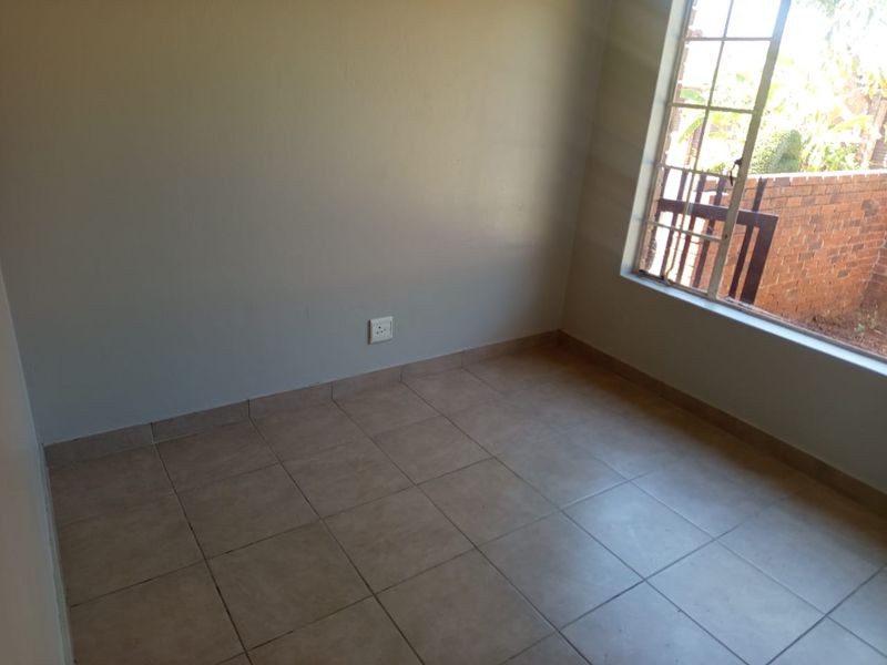 An empty bedroom featuring tiled flooring and a window with security bars, providing a blank canvas for personalization.