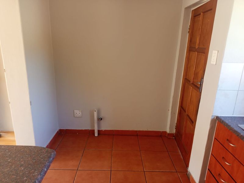 A dedicated laundry area featuring tiled flooring, plumbing connections for a washing machine, and a wooden door.
