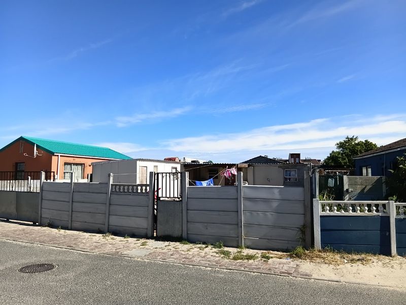 Front view of a residential property featuring a precast concrete boundary wall, metal gate, and paved street frontage.
