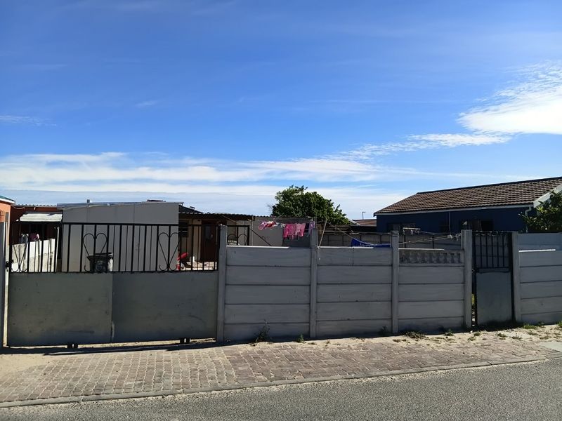Front view of a residential property featuring a precast concrete boundary wall, metal sliding gate, and paved street-side verge.