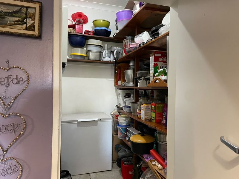 A functional scullery or pantry area featuring extensive built-in timber shelving for storage and space for a chest freezer.