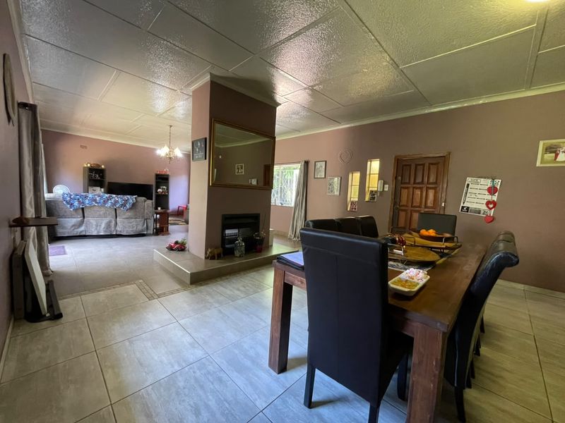Spacious open-plan living and dining area featuring tiled flooring, a central built-in fireplace, and a panel ceiling.