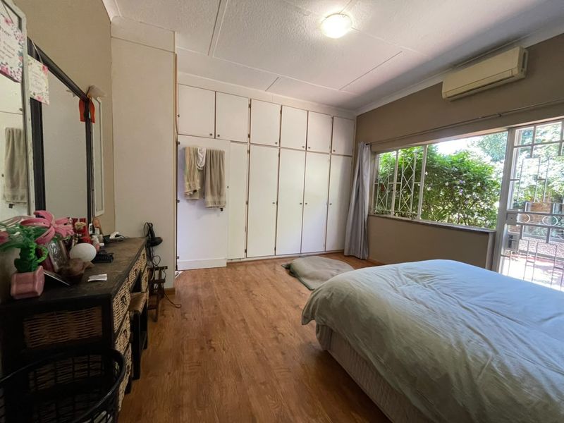 Spacious bedroom featuring extensive built-in cupboards, laminate flooring, and a split-system air conditioner with direct access to the garden area.