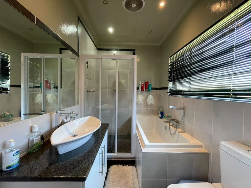 A well-appointed bathroom featuring a vessel sink on a granite vanity, a separate shower enclosure, a built-in bathtub, and modern tiled finishes.