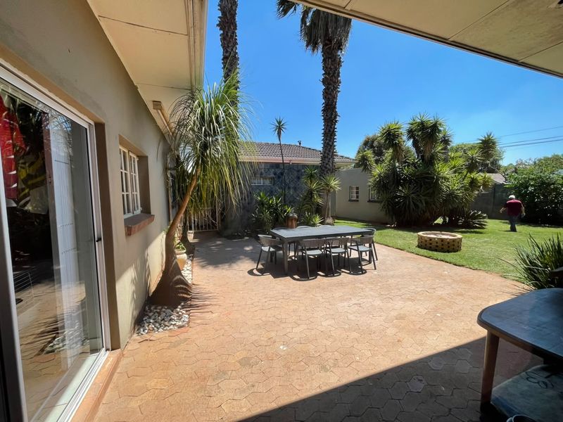 A covered outdoor patio area featuring paved flooring, direct access to the home via sliding glass doors, and an adjacent garden with a fire pit.
