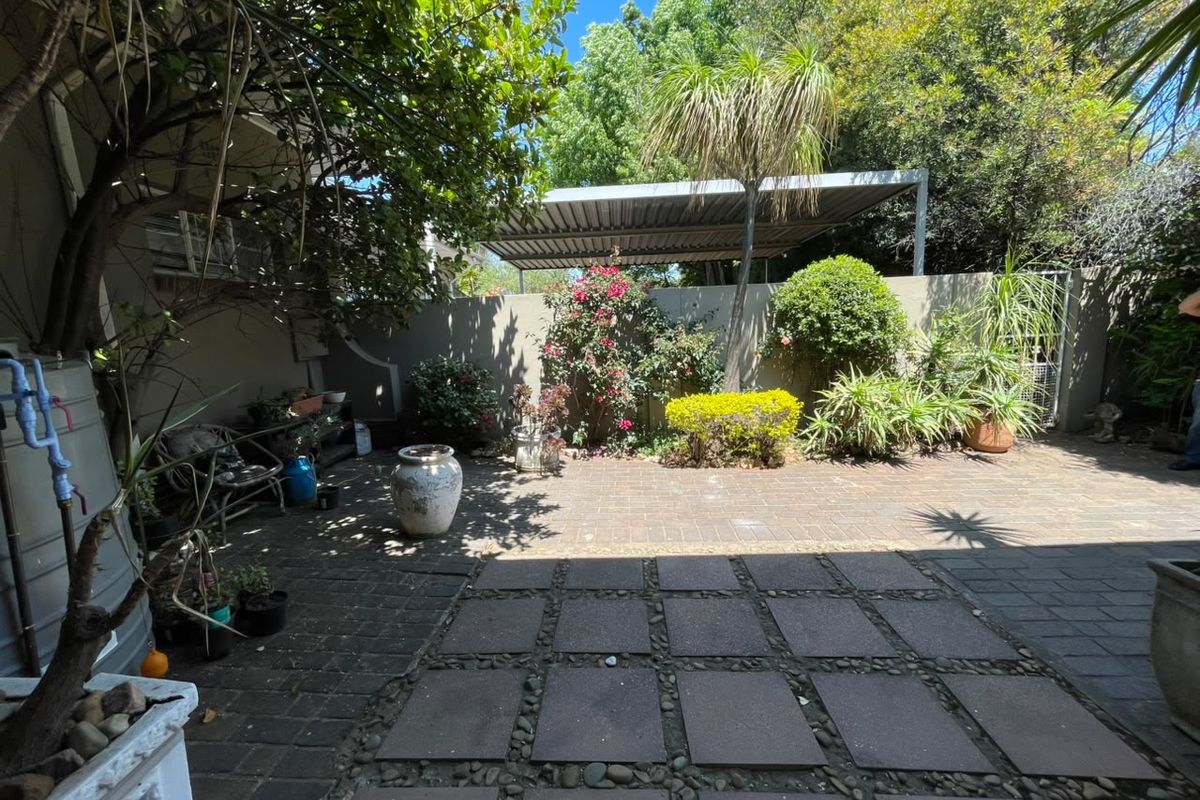 A private rear courtyard featuring paved flooring, a covered carport, and established garden landscaping.