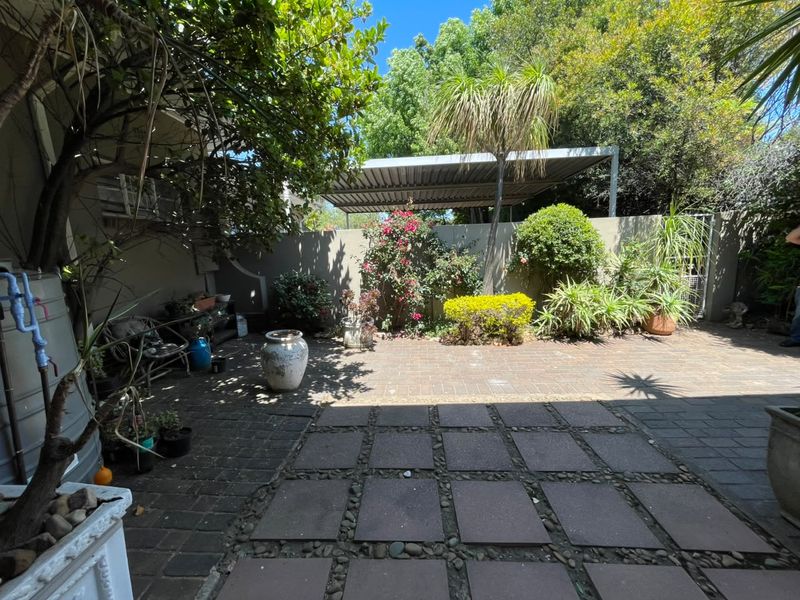 A private rear courtyard featuring paved flooring, a covered carport, and established garden landscaping.