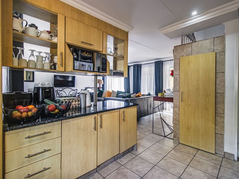 Open plan kitchen featuring light wood cabinetry, granite countertops, and built-in microwave, flowing seamlessly into the adjacent living area with tiled flooring throughout.