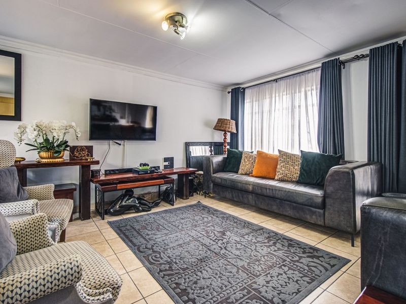 A comfortable living room featuring tiled flooring and large windows with curtain rails, providing a functional and well-lit space for relaxation.